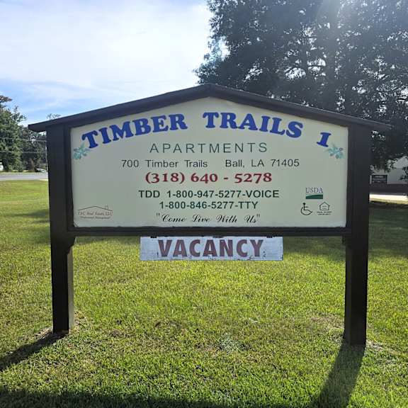 a sign for timber trails apartments with a vacancy sign on it.