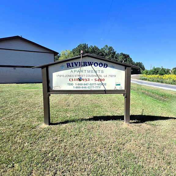 a sign for riverwood apartments is displayed in a grassy area.