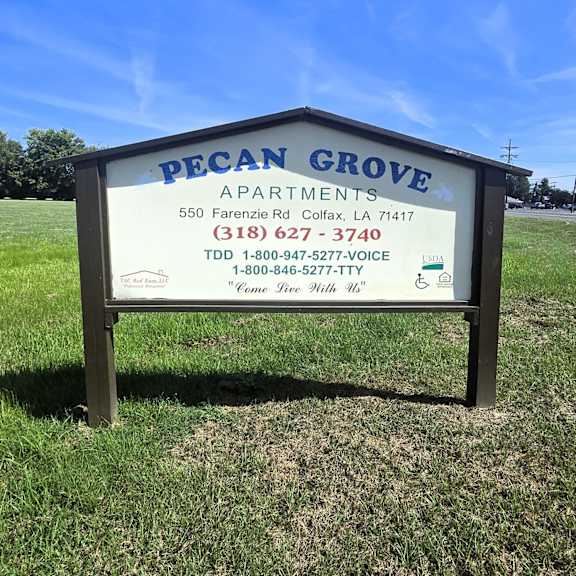a sign for pecan grove apartments is displayed in a grassy area.