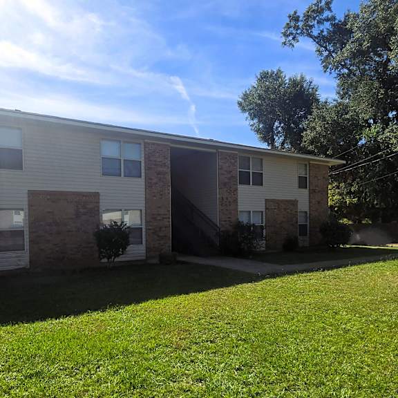 a two-story brick apartment building with a green lawn in front.