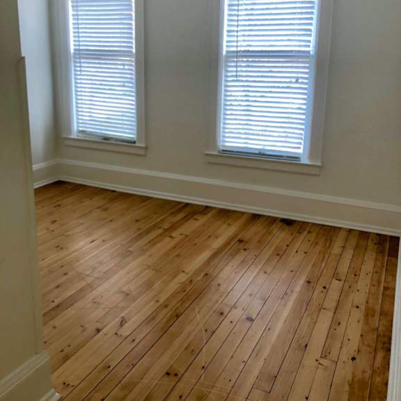 a room with wooden floors and two windows.