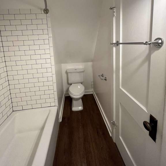 a white toilet sits in a small bathroom with a white bathtub and a white door.