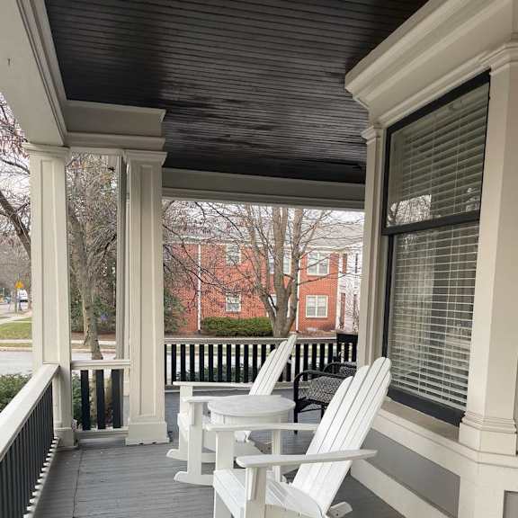 a porch with white rocking chairs and a black railing.