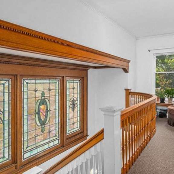 a bradley veneklase stained glass window is on the left side of a wooden staircase.