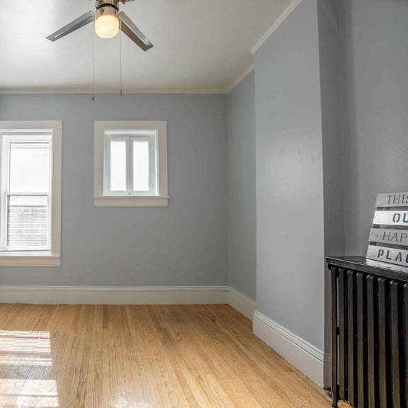 a room with a ceiling fan and two windows.