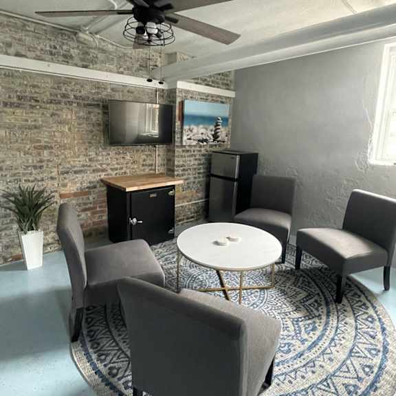 a room with a ceiling fan, a table with chairs, and a brick wall.