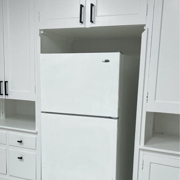 a white refrigerator is in a kitchen with white cabinets.