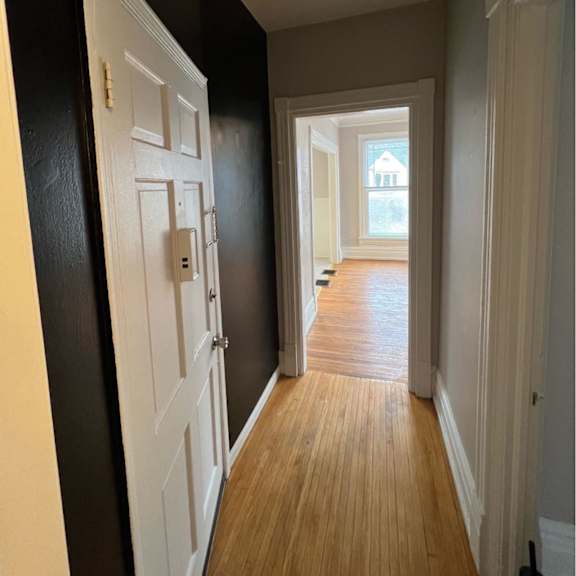 a hallway with a white door on the left and a wooden floor.