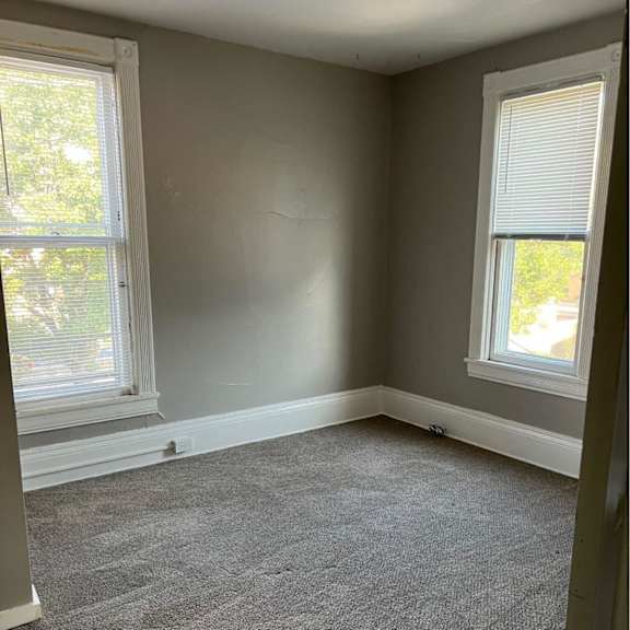a room with grey carpet and two windows.