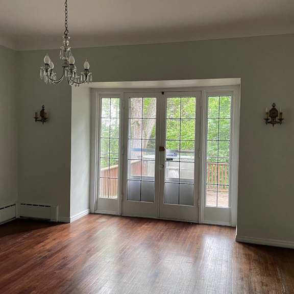 a room with a chandelier and a view of a tree-lined street through the glass doors.