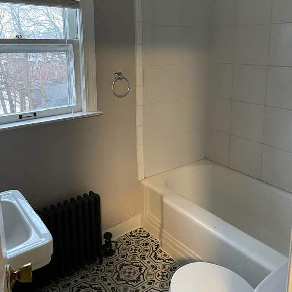 a bathroom with a black and white floor, a white tub, and a window.