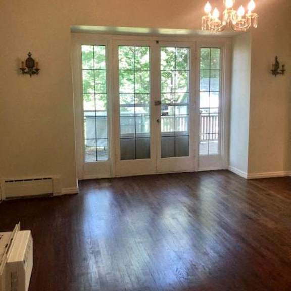a room with a chandelier, a window with a view of a balcony, and a wooden floor.