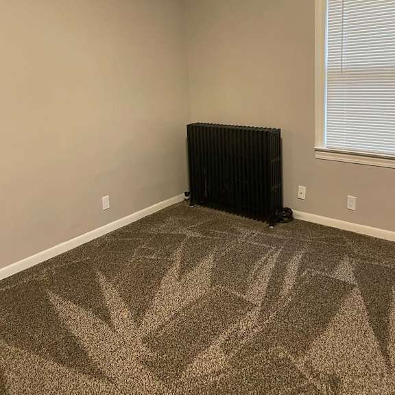 a black radiator is in the corner of a room with a window and a carpet with a leaf design.