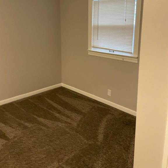 a room with a carpeted floor and a window with blinds.