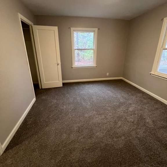 a room with a carpeted floor, a window, and a door.