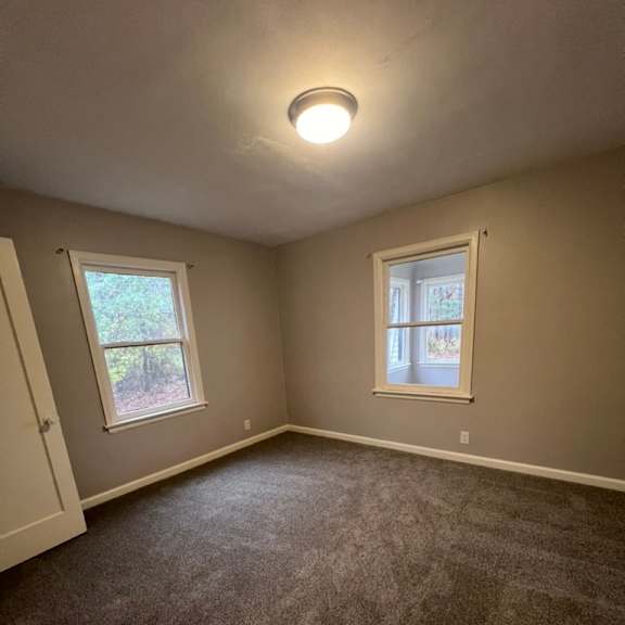 a room with carpeted floor and two windows.