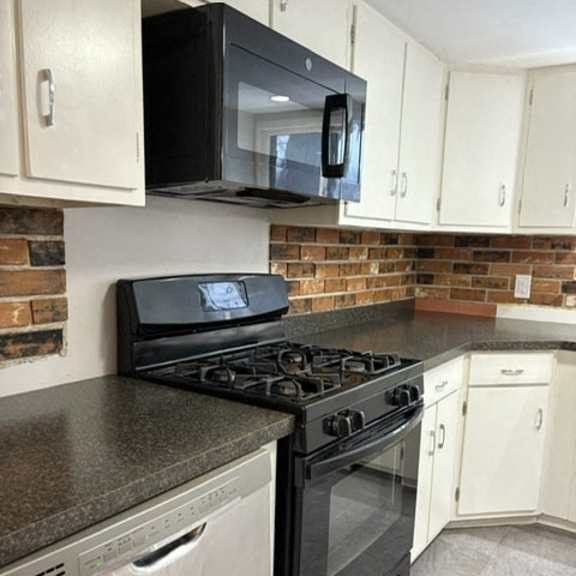 a black microwave is mounted above a black stove in a kitchen with white cabinets.