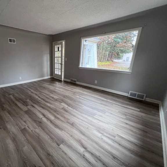 a room with wooden flooring and a window showing trees outside.