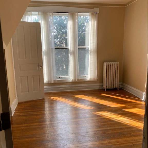 a room with wooden floors and a window with white curtains.