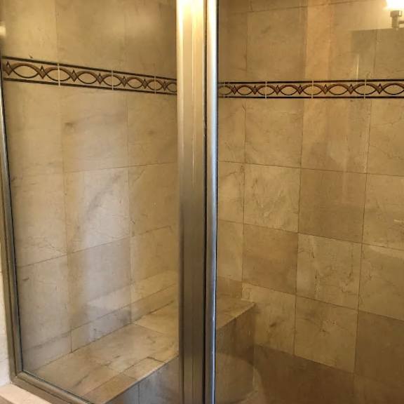 a shower with a glass door and tiled walls.
