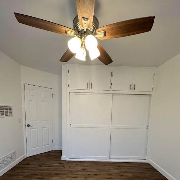 a room with a ceiling fan and light fixture, and a wooden floor.
