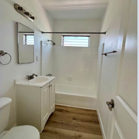 a white bathroom with wood flooring and a white toilet.