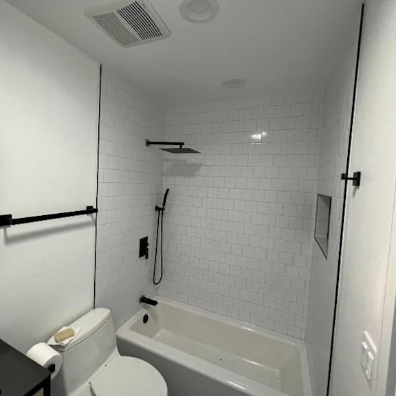 a white tiled bathroom with a toilet, sink, and bathtub.
