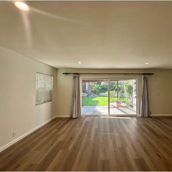 a room with wooden floors and a large window with a view of a green lawn.