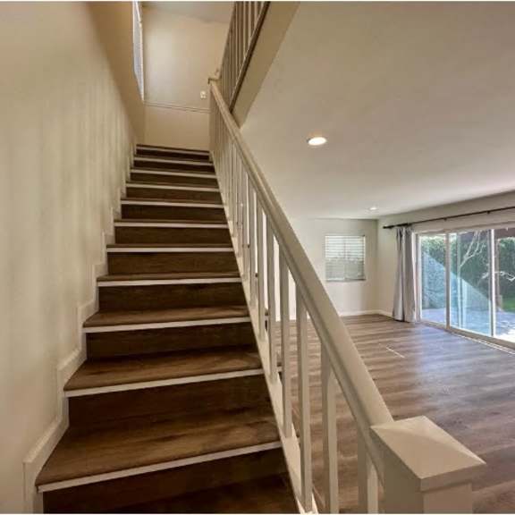 a staircase with wooden steps and white railings leads to a bright room with sliding glass doors.