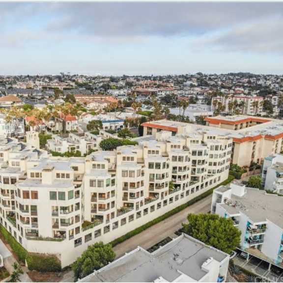 a large white apartment building with balconies is surrounded by other buildings and trees.