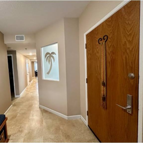 a long hallway with a door on the right and a picture of a palm tree on the wall.