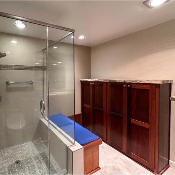 a glass shower stall with a blue bench and a glass door.