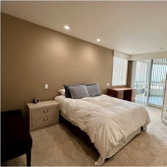 a bedroom with a large bed, nightstand, and a window with blinds.