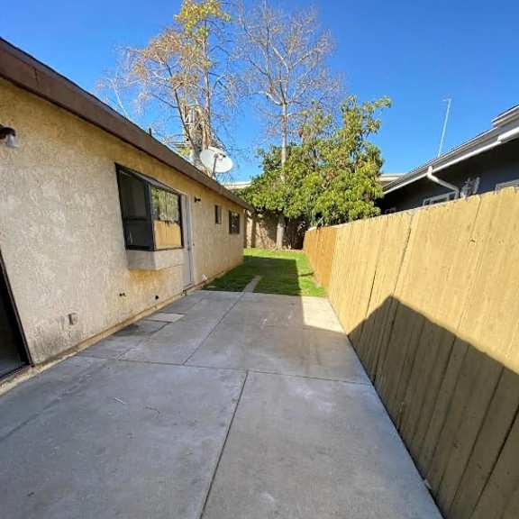 a concrete driveway leads to a house with a wooden fence on the right.
