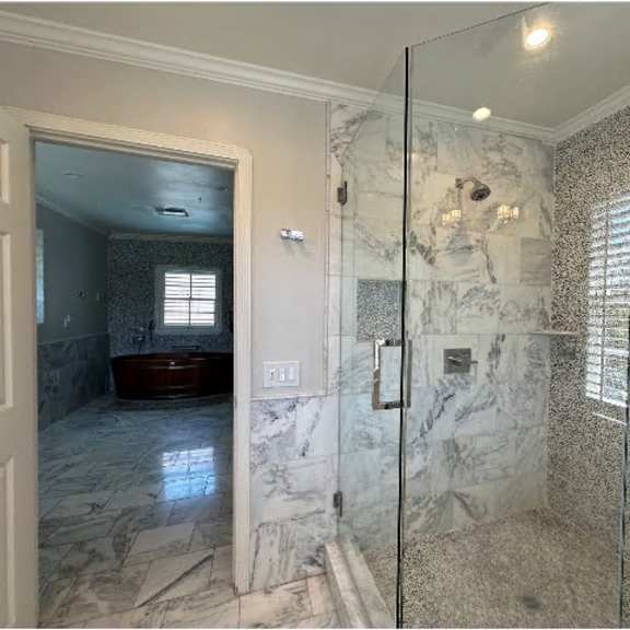 a bathroom with a marble tile shower and a glass door.
