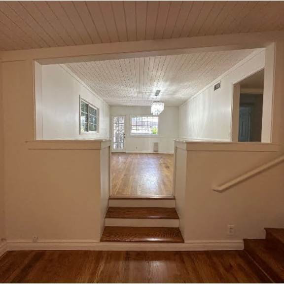a hallway with wooden floors and white walls leading to a staircase.