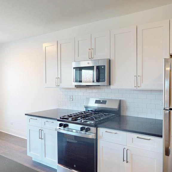 a modern kitchen with a stainless steel refrigerator and black countertops.