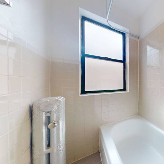 a white bathtub sits in a bathroom with a window above it.