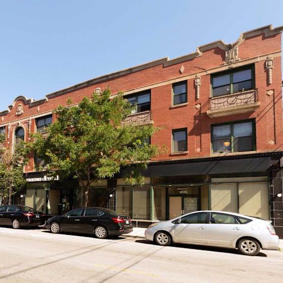 a row of parked cars on a street in front of a red brick building.