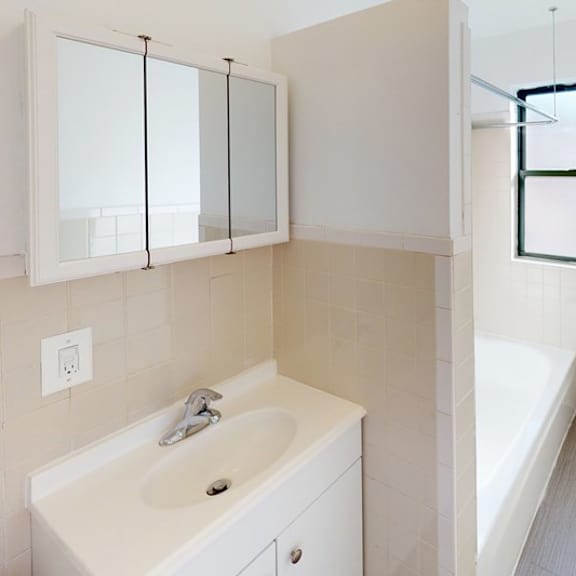 a white bathroom with a sink, mirror, and bathtub.