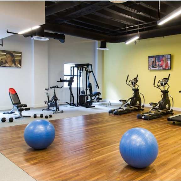 a gym with a variety of equipment including treadmills, stationary bikes, and exercise balls.