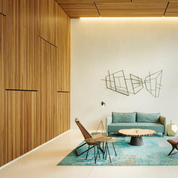 a modern living room with a blue rug and a large abstract metal sculpture on the wall.