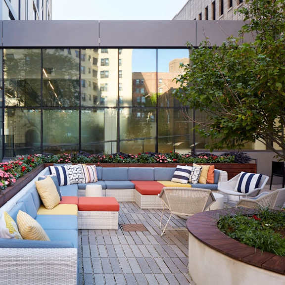 a patio with a couch and chairs is surrounded by flowers.