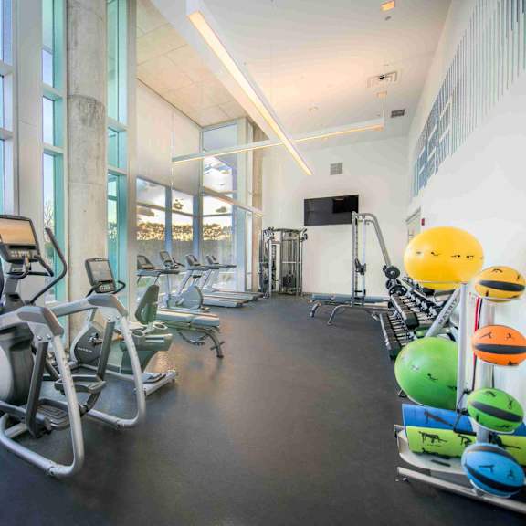 a gym with treadmills, elliptical machines, and exercise balls.