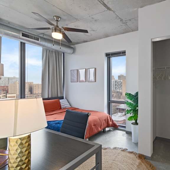 a bedroom with a bed, a ceiling fan, and a view of the city.
