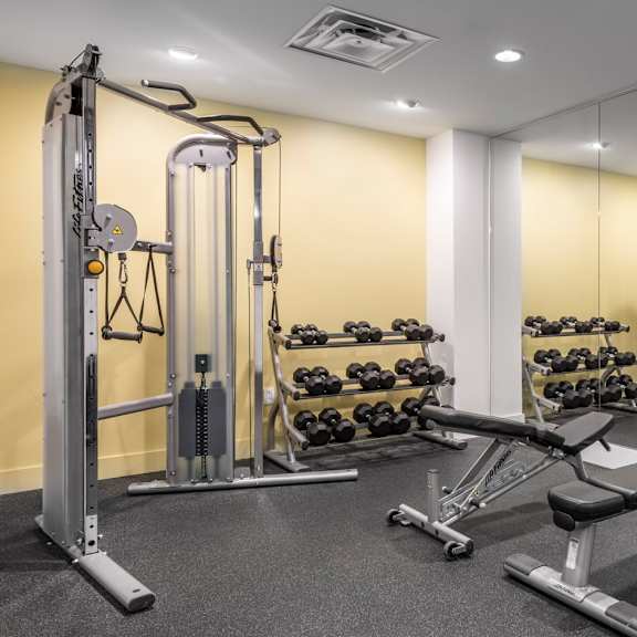 a gym with a variety of equipment including a leg press machine, dumbbells, and a bench press.