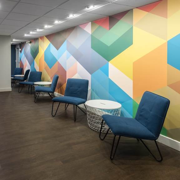 a hallway with blue chairs and a colorful wallpaper.