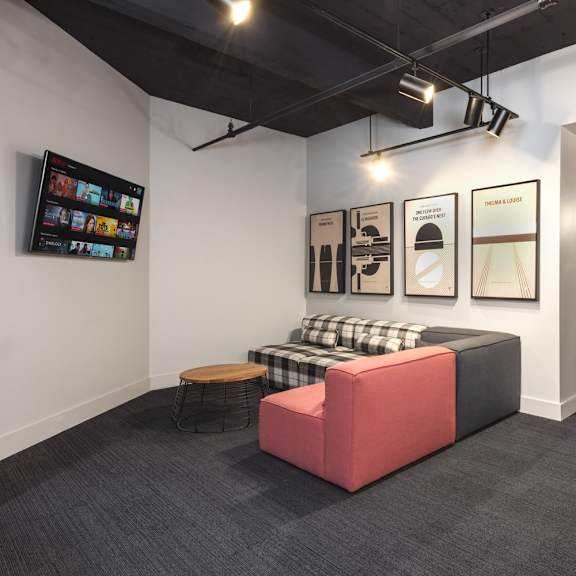 a room with a red couch, a black and white checkered ottoman, a tv, and a dining table with chairs.