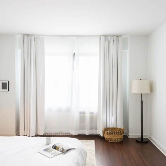 a white bedroom with a large bed and a window with curtains.