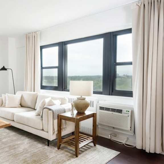 a living room with a white couch, a wooden coffee table, and a large window with a view of the outdoors.